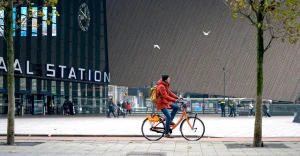 Fieter die op een Donkey Replubic fiets voor Rotterdam Centraal langsfiets. Foto afkomstig van Rotterdam.info