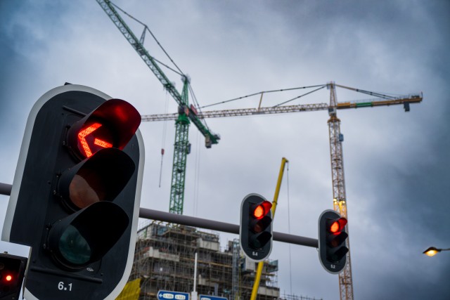 Drie verkeerslichten op een rij die allemaal op rood staan, erachter zijn bouwkranen te zien