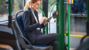 Een vrouw die een woon-werkreis afgelegd met de bus en op haar smartphone aan het lezen is