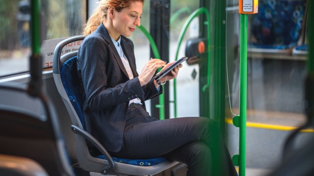 Een vrouw die een woon-werkreis afgelegd met de bus en op haar smartphone aan het lezen is