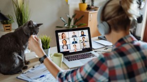 Een vrouw die thuis aan haar bureau aan het thuiswerken en via haar laptop aan een digitaal overleg deelneemt